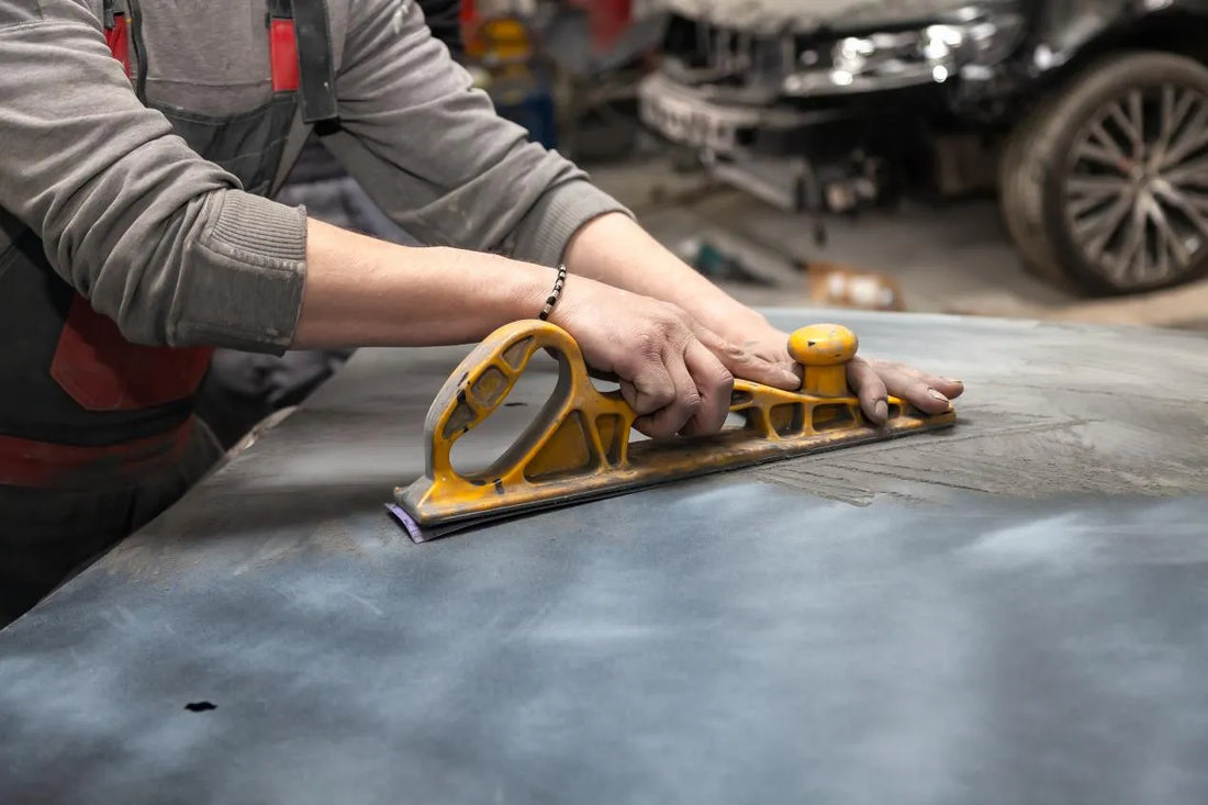 A man is sanding the car part with a sanding block