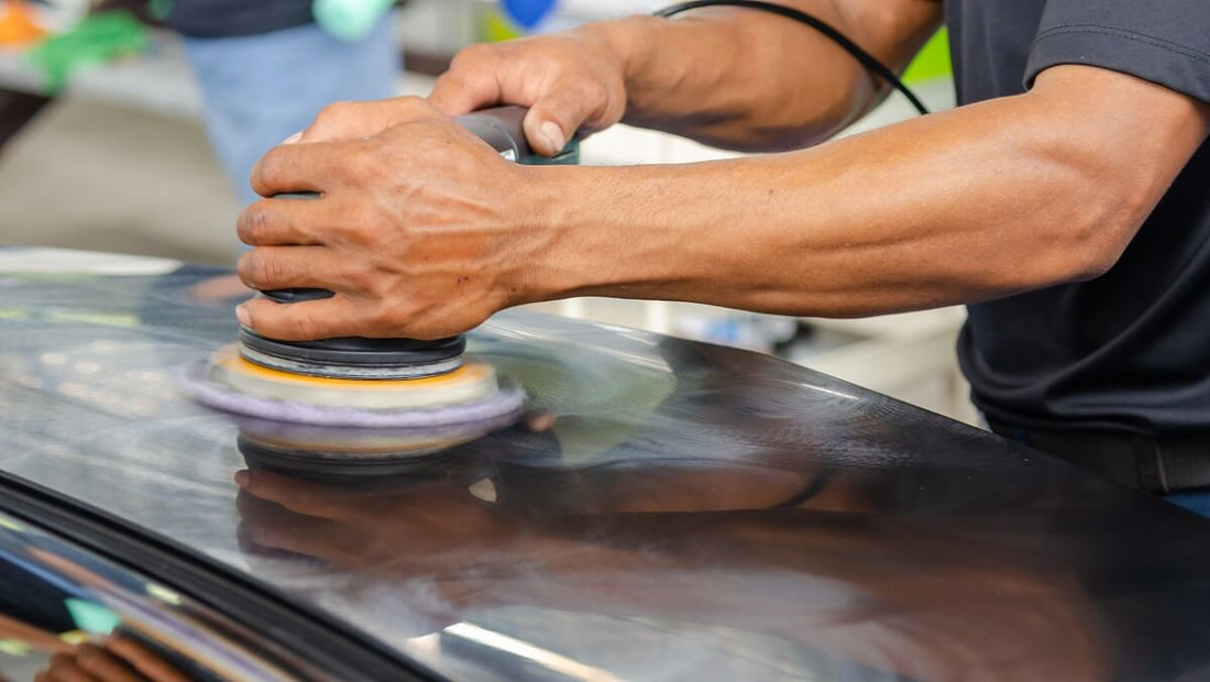 A car mechanic is sanding the car surface using a random orbital sander